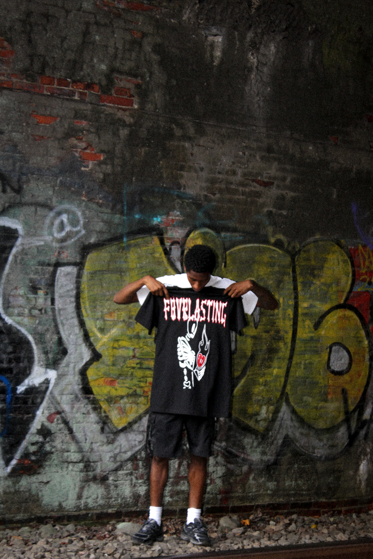 F8VRLASTING black skeleton tee held up against a graffiti wall